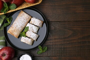 Tasty apple strudels with powdered sugar, mint and fruits on wooden table, flat lay. Space for text