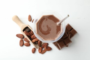 Tasty chocolate milk, bars and cocoa beans on white wooden table, flat lay