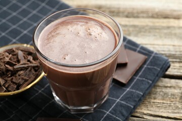 Tasty chocolate milk with shavings and pieces on wooden table, closeup