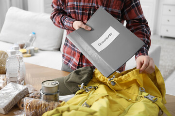 Survival kit. Woman putting documents into backpack at table indoors, closeup