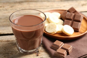 Tasty chocolate milk, pieces and banana on wooden table, closeup