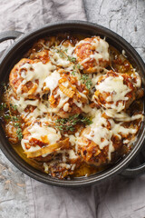 French onion meatballs smothered in rich caramelized onion gravy and topped with melty Gruyere cheese closeup on the pan on the table. Vertical top view from above