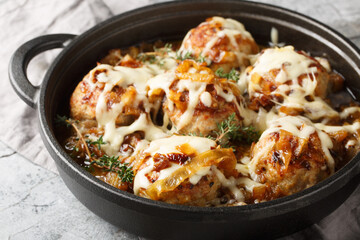 Skillet dinner inspired by the iconic French onion soup with caramelized onions, meatballs, and gooey cheese closeup on the table. Horizontal