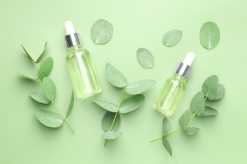Bottles of essential oil and eucalyptus leaves on green background, flat lay