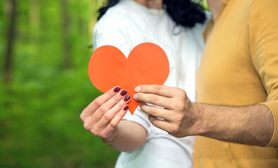 Heart as a symbol of love. Close up of a red heart holding the hands of a man and a woman together.