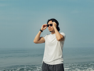 Obraz premium Man wears white t-shirt and sunglasses enjoy walking on the beach.