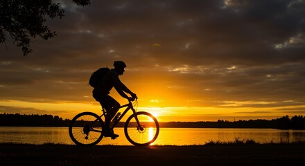 Fototapeta premium Silhouette of cyclist enjoying a golden sunset by a lake.