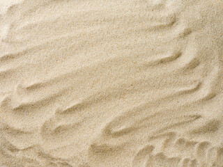 Beach sand background with natural wave pattern. Summer background of beach sand with small stones along the edges. Tourism, vacation and holidays concept. Top view.