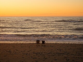 Two empty camping chairs on Gillespies Beach with ocean waves in the background during sunset West...