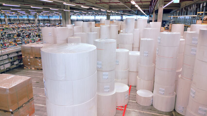 A vast warehouse reveals massive stacks of white rolls and cardboard boxes, symbolizing global...