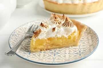 Piece of delicious pie with browned meringue and fork on white wooden table, closeup