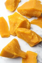 Pieces of natural beeswax for making candles on white marble table, closeup