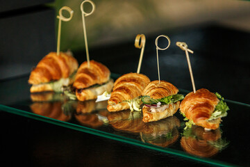 Four small croissant sandwiches held together by skewers with looped tops, placed on a glass...