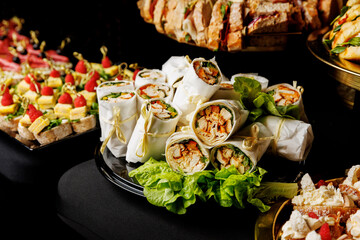 A vibrant spread of wraps filled with vegetables and chicken, tied with string and garnished with lettuce on a decorative platter at event catering