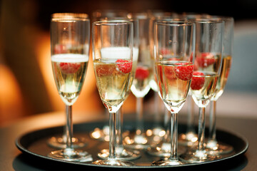 Elegant champagne flutes filled with sparkling wine, each garnished with fresh raspberries, arranged neatly on a serving tray.