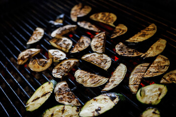 Close-up of sliced eggplant and zucchini cooking on a hot charcoal grill. Fresh vegetables with char marks sizzling over open flames.