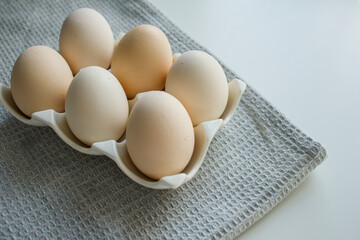 Fresh farm chicken eggs on a white ceramic egg tray and grey kitchen towel