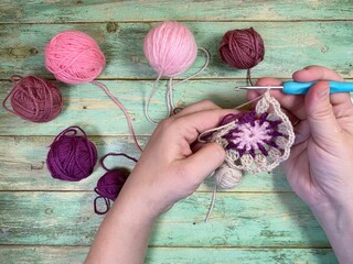 Female hands and process of crocheting of colorful mandala doily round object, yarn, clews and crochet on wooden background	
