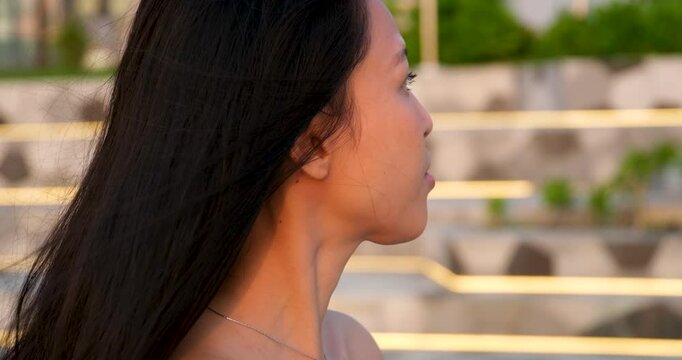 Attractive Asian woman looks sideways, shows facial profile in sunlight. Closeup, slowmotion shot.