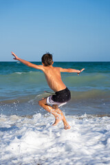 Fototapeta premium Boy jumping into ocean waves with outstretched arms, enjoying summer vacation