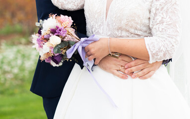 dos novios abrazados juntando sus manos y enseñando el ramo de flores de la novia, el novio la...