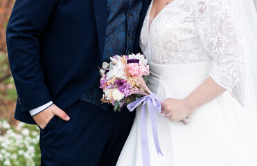 dos novios abrazados juntando sus manos y enseñando el ramo de flores de la novia, el novio la...