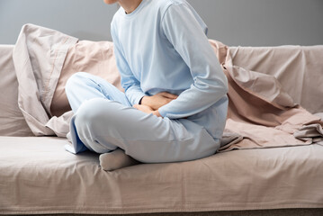 Girl in pajamas holding her stomach. Menstruation. Abdominal pain, hands of a woman with abdominal pain due to menstruation, diarrhea or constipation.
