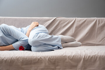 A girl in blue pajamas holds her stomach. There is a red rose next to her as a symbol of menstruation. Depression