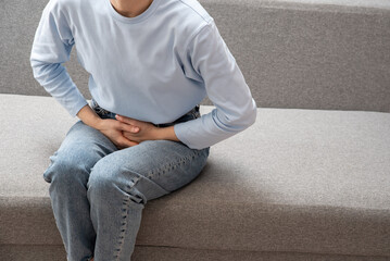 Girl in pajamas holding her stomach. Menstruation. Abdominal pain, hands of a woman with abdominal...