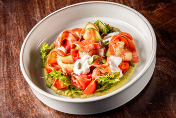 A beautifully arranged salad featuring thinly sliced vegetables, fresh tomatoes, and a drizzle of creamy dressing. The vibrant colors and textures create an appealing and healthy dish.
