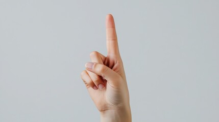 Close up of an adult hand pointing up with one index finger, indicating number one or specific direction against plain grey background, showing clear, neutral pointing gesture