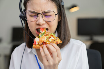 Asian businesswoman eating pizza while working with clients due to rush hour.