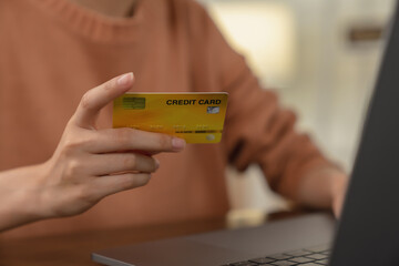 Close-up of hand holding yellow credit card and type on laptop keyboard with online payment for shopping.