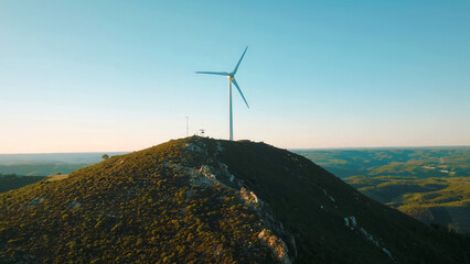 A wind turbine stands atop a mountain with a clear blue sky in the background, symbolizing renewable energy, clean power, and sustainable technology in a natural landscape