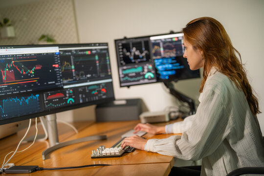 Young woman analyzes financial data on multiple computer screens in modern office setting during daytime