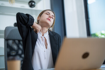 Young professional feeling neck pain while working at a desk in a modern office environment during...
