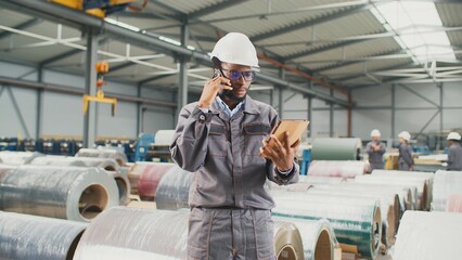 Busy African American worker accepting order from client for manufacture of industrial goods. Serious man talking on phone while entering customer data into tablet. Working with technology in plant.