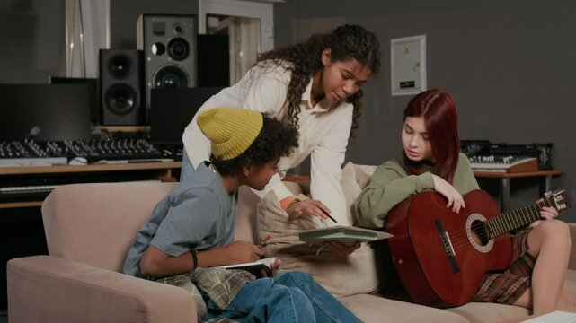 Boy singer with notebook and girl with acoustic guitar listening to inspired teenage musician presenting lyrics for new composition in recoding studio