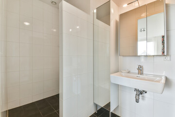 This image showcases a sleek and contemporary bathroom with elegant white tiles and a stylish sink, enhancing its spacious feel and cleanliness.