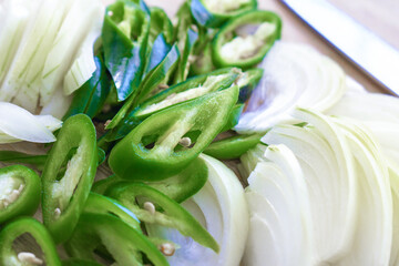 Green chilli pepper and onion slices with a knife on chopping board.