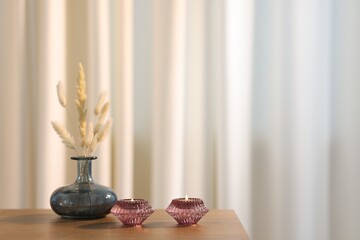 Stylish candlesticks with burning candles and dry spikes on wooden table indoors, space for text