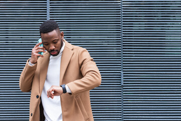 African American man checking time while making phone call close up, confident positive businessman planning meeting with partner, looking at wristwatch, task management