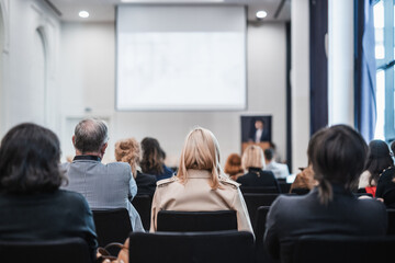 Fototapeta premium Speaker giving a talk in conference hall at business event. Rear view of unrecognizable people in audience at the conference hall. Business and entrepreneurship concept
