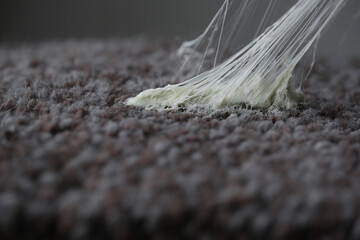 Sticky substance stretching on gray textured carpet. Removing chewing gum from carpet