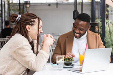 Two happy friends sharing a brunch together while working with laptop in the eco coffee shop terrace