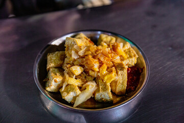 Plate of Taiwanese stinky tofu topped with pickled cabbage and chili sauce, served in a metal dish at a street food stall
