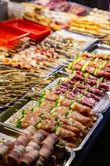Close-up of assorted raw meat skewers including chicken, beef and vegetables, neatly arranged on trays at a vibrant Taiwanese night market