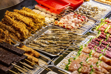 Street food vendor's display of various skewers including grilled fish, fried tofu, bacon wraps, and rolled bean curd, ready for customers at a Taiwanese night market