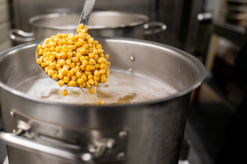 A metal ladle scoops tender yellow split peas from a pot of boiling water. The steam rises, showcasing a vibrant cooking scene in a professional kitchen, highlighting nutritious food preparation.