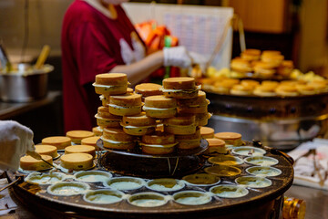Taiwanese street vendor preparing stacks of traditional red bean cakes on a circular griddle, cakes in different cooking stages